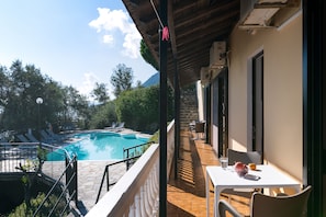 A balcony with a pool view, a table with a bowl and a glass, and a chair.