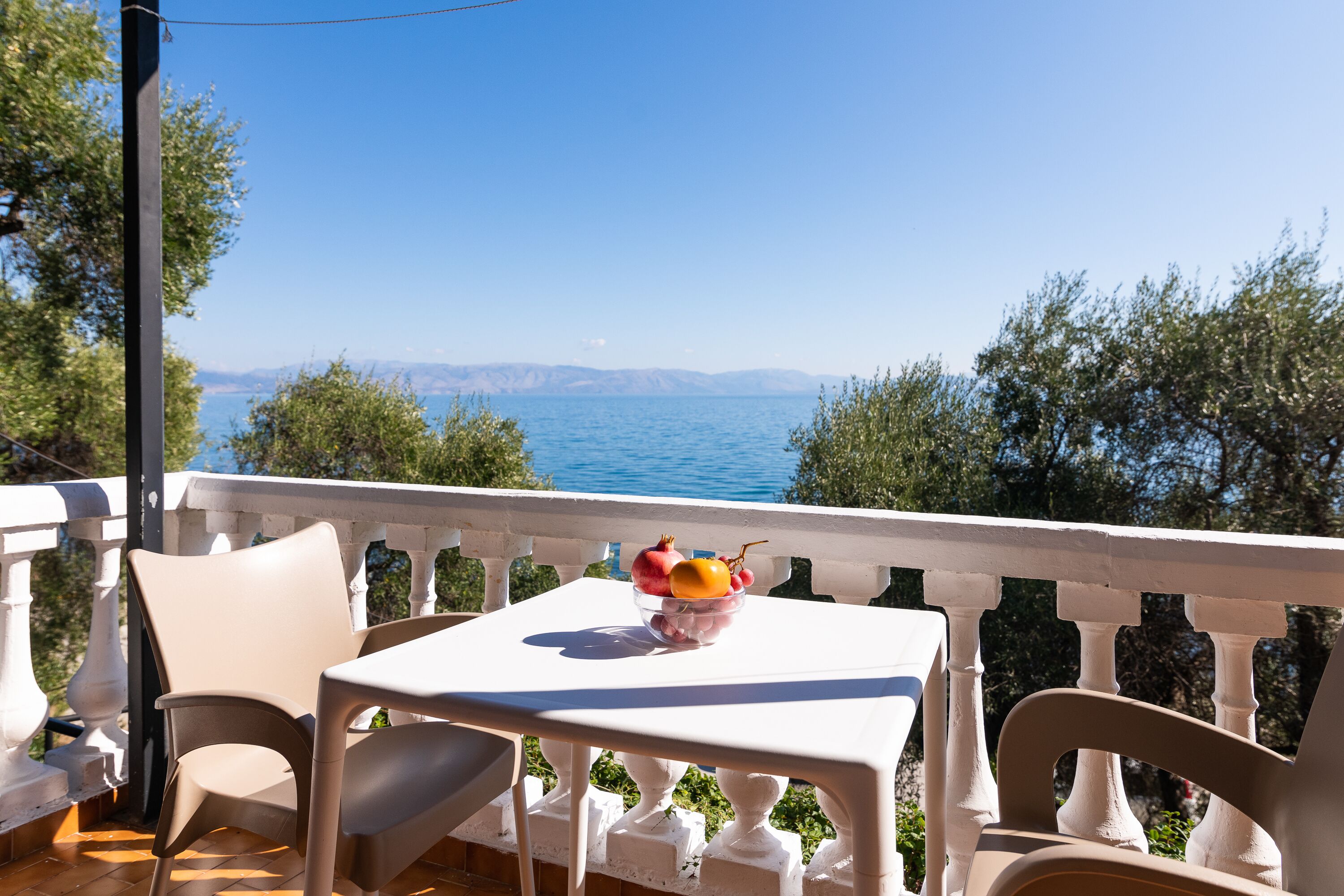 A balcony with a table and chairs, overlooking a body of water and distant mountains.