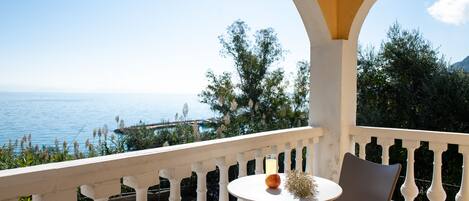 Varanda com vista para o mar, uma mesa com um copo de bebida e uma fruta, e duas cadeiras.