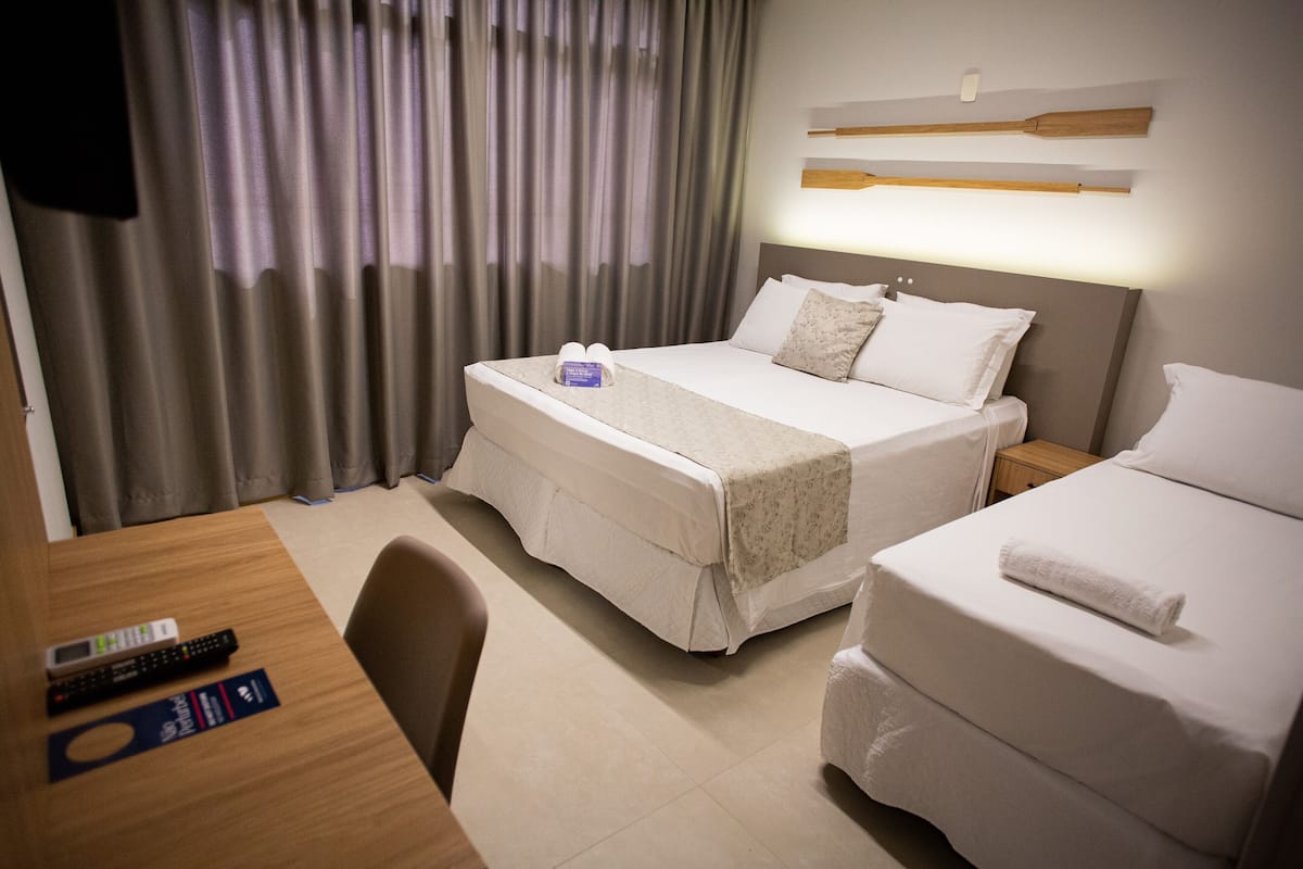 Ein Hotelzimmer mit zwei Betten, einem Schreibtisch mit Fernbedienung und Vorhängen.