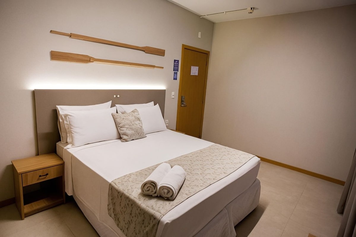 Una habitación de hotel con una cama, una mesita de noche, un cabecero de madera y una puerta.