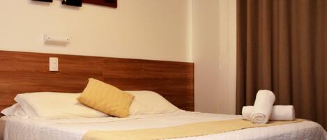 A hotel room with two beds, a wooden headboard, a beige blanket, and a brown curtain.