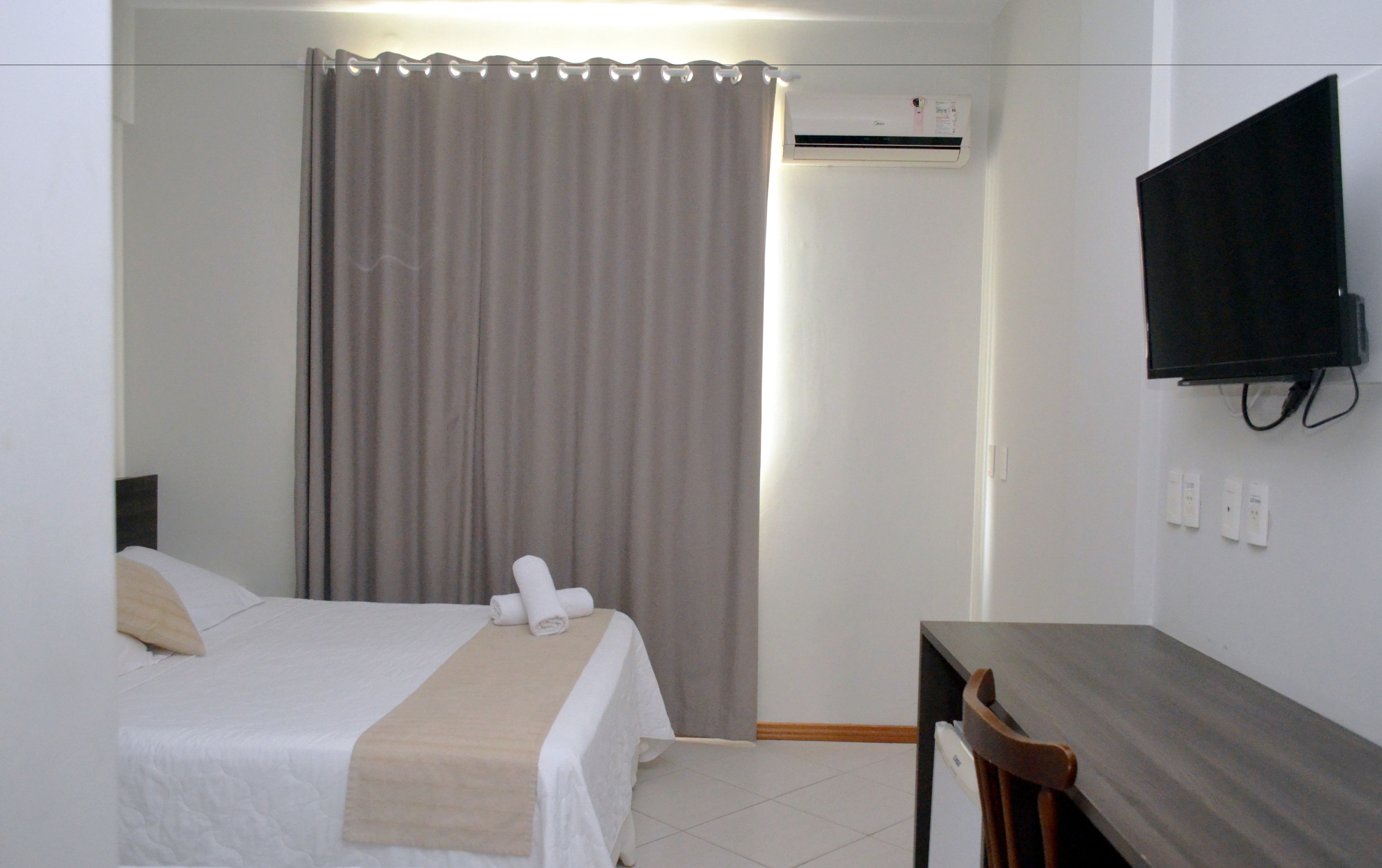 Quarto de hotel com uma cama, uma mesa, uma televisão e um aparelho de ar condicionado.