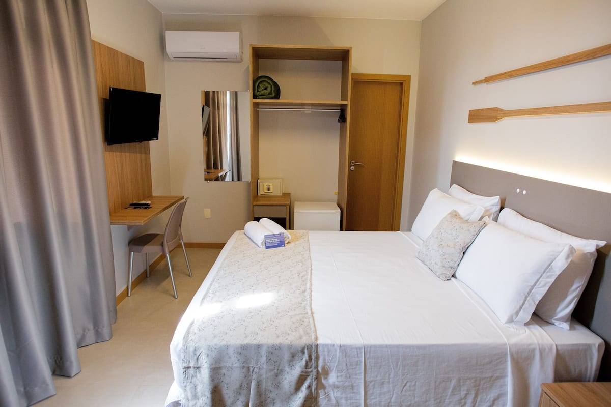 Ein Hotelzimmer mit Bett, Schreibtisch, Stuhl, Fernseher, Kleiderschrank und einem kleinen Tisch.