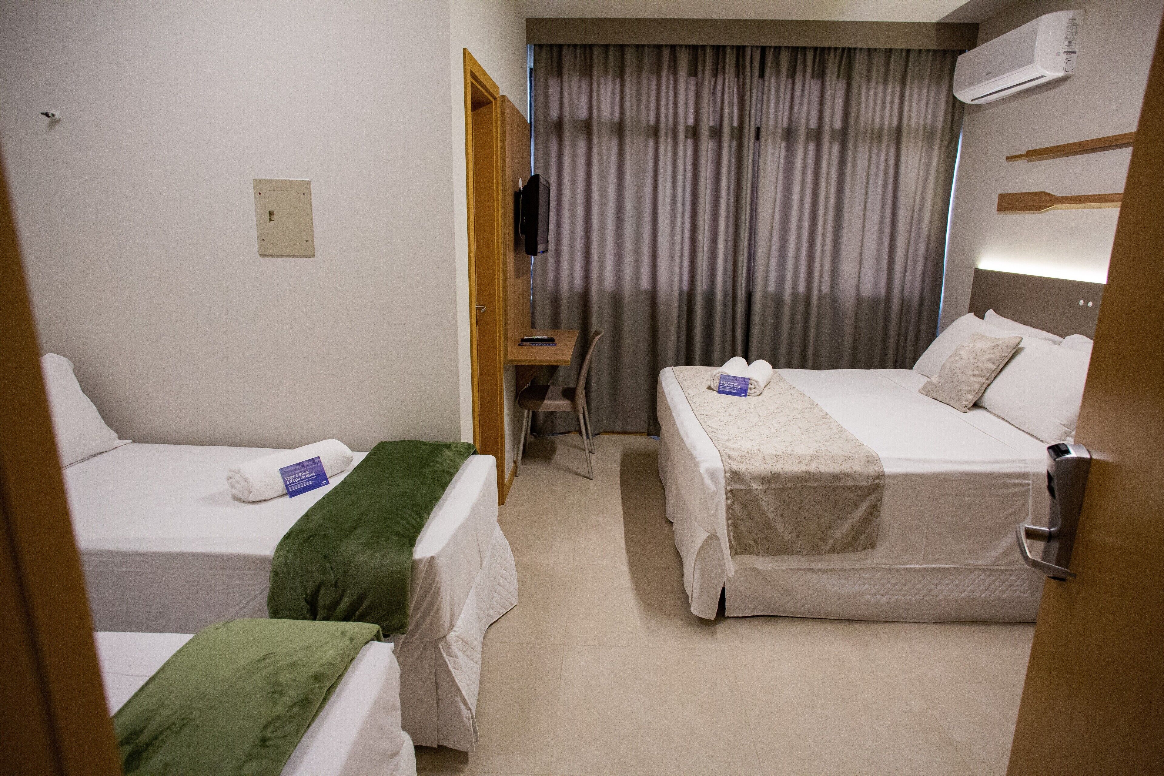 Habitación de hotel con dos camas individuales, un escritorio, una silla y una ventana con cortinas.