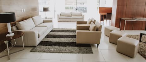 A modern living room with a sofa, armchairs, ottomans, a coffee table, and a rug.