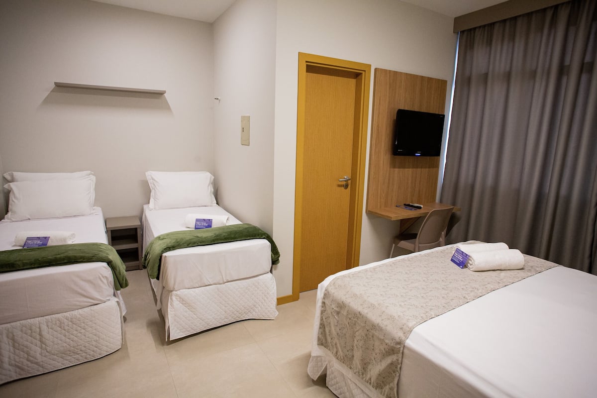 Ein Hotelzimmer mit zwei Einzelbetten, einem Schreibtisch, einem Fernseher und einer Tür.