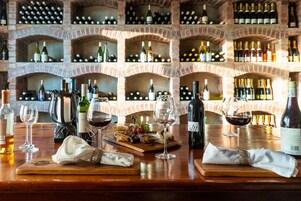 Disposición para una cata de vinos con botellas y copas sobre una mesa de madera, rodeada por una bodega de ladrillo.