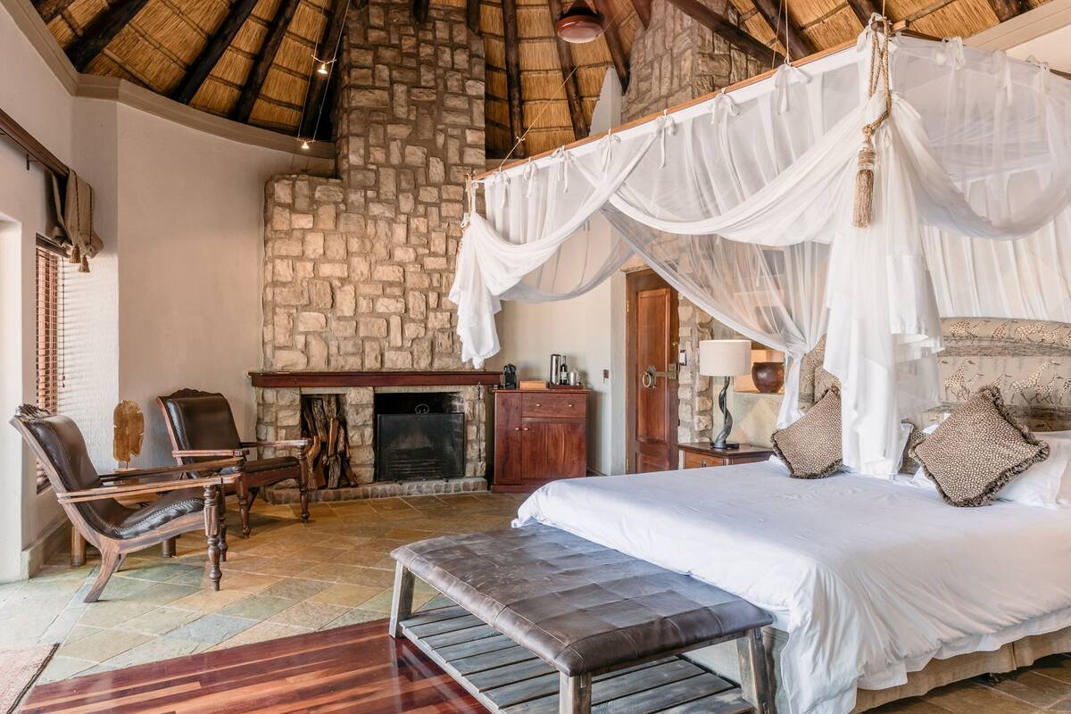 A bedroom with a stone fireplace, a canopy bed, and a bench.