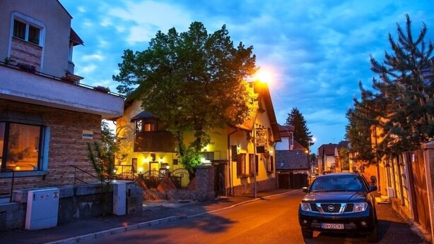 A street view at dusk with a parked SUV, a building with a sign reading "ALCIMIE," and a tree-lined road. - Pension Brasovu' Vechi (Brasov)