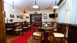 A dining area with wooden tables and chairs, a red carpet, and pendant lighting. - Pension Brasovu' Vechi (Brasov)