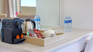 Hotellihuoneen työpöydällä on kahvinkeitin, vesipulloja, kahvipannu ja tarjotinalus, jossa on pientä purtavaa.