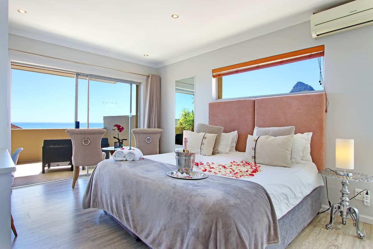 A spacious bedroom with a large bed, a desk, and a chair. There is a view of the ocean through large windows.