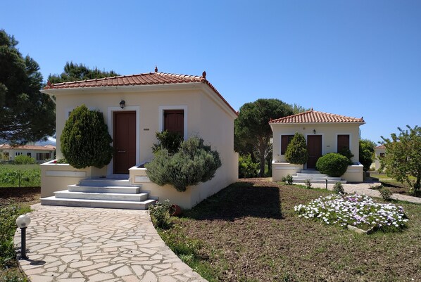 Two small, single-story buildings with tiled roofs and white walls, each with a front door and steps leading to the entrance. - Gaea Gardens Studios (Lesvos)