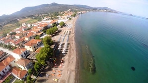 An aerial view of a coastal town with a beach lined with umbrellas and sun loungers. - Gaea Gardens Studios (Lesvos)