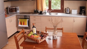 A kitchen with wooden cabinets, a microwave, a sink, and a dining table with chairs. - Gaea Gardens Studios (Lesvos)