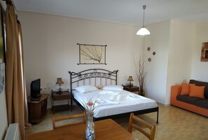 Un dormitorio ordenado con cama, mesitas de noche, televisor, una mesa de comedor y un jarrón con flores.