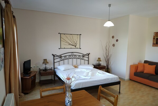 Un dormitorio ordenado con cama, mesitas de noche, televisor, una mesa de comedor y un jarrón con flores.