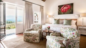 A bedroom with a bed, two chairs, a nightstand, a lamp, and a painting. - Galenia Estate (Montagu)