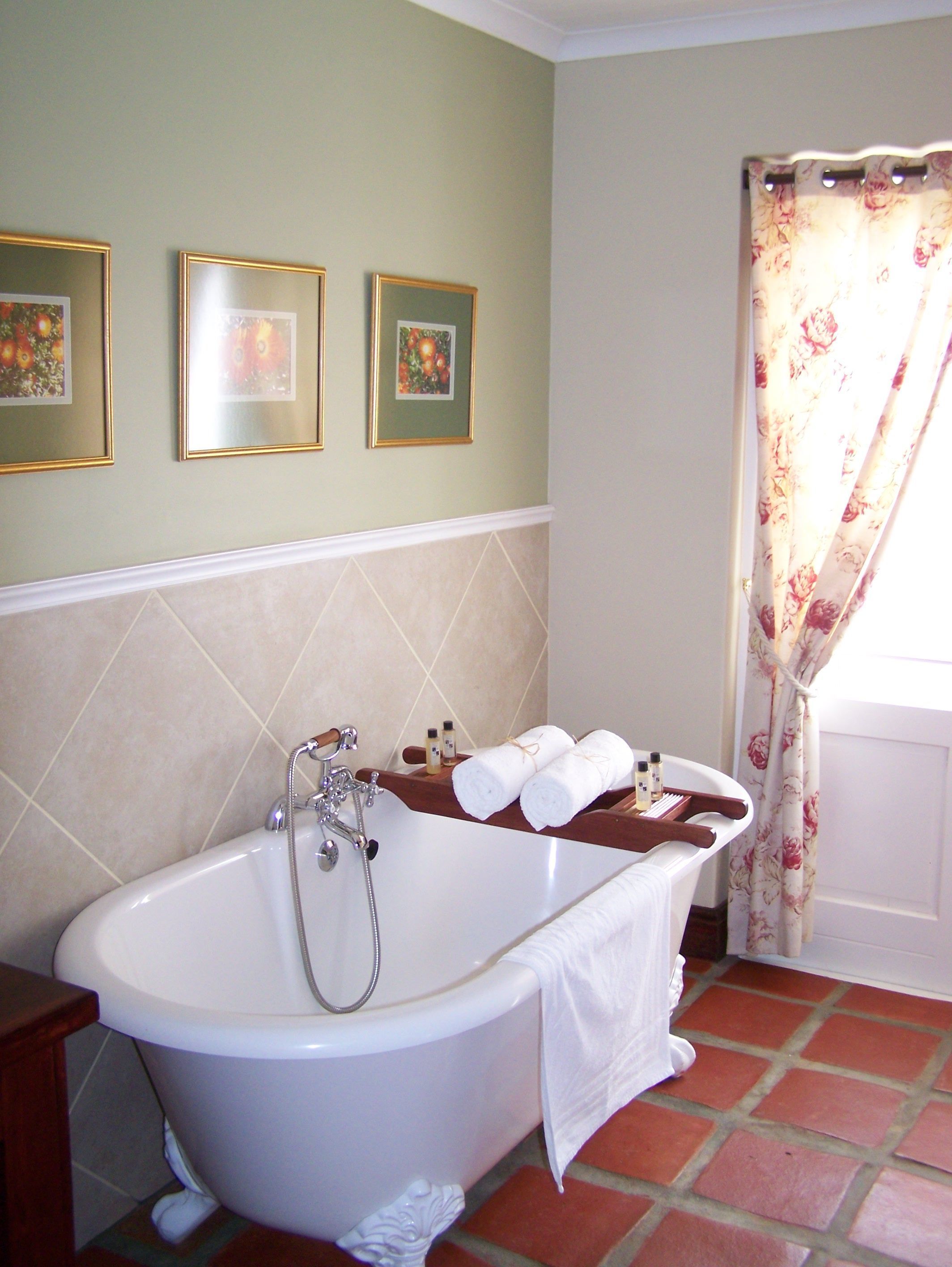 Un baño con una bañera independiente, ducha y retrete. Hay tres cuadros enmarcados en la pared, un perchero con toallas y una cortina con estampado floral.