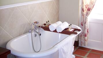 Un baño con una bañera independiente, ducha y retrete. Hay tres cuadros enmarcados en la pared, un perchero con toallas y una cortina con estampado floral.