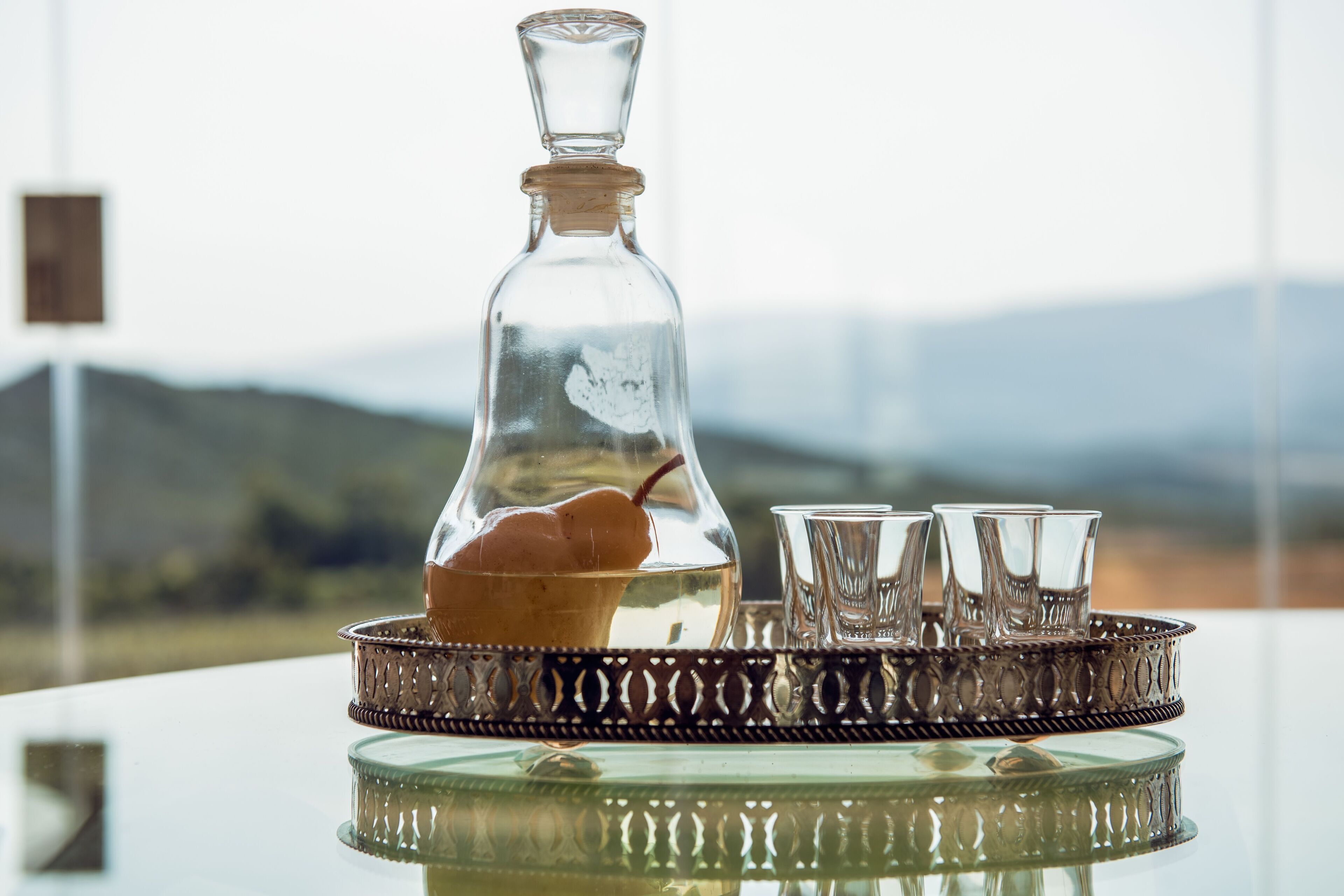A clear glass decanter with a cork stopper, a metal tray with a decorative pattern, and four clear glasses on the tray.