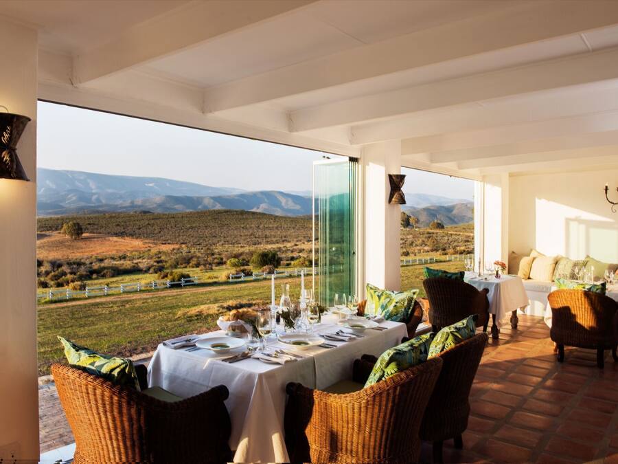 A dining area with a table set for two, overlooking a scenic landscape with mountains and a fence.