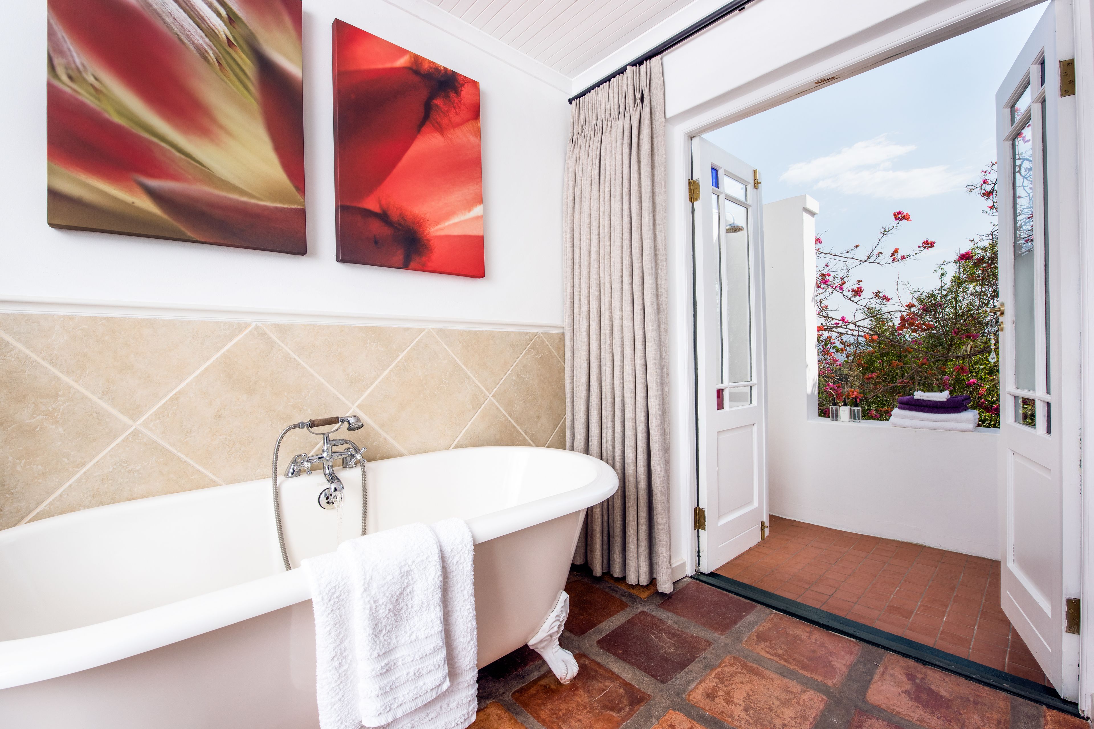 A bathroom with a freestanding bathtub, a tiled shower area, and a view of a garden through an open door.
