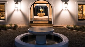 A building with a central arched entrance, a fountain in front, and two wall-mounted lights. - Galenia Estate (Montagu)