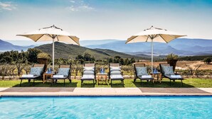 A poolside area with lounge chairs and umbrellas, a clear view of distant mountains, and a pool. - Galenia Estate (Montagu)