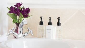 A bathroom sink with a modern faucet, three bottles of Charlotte Rhyss body lotion, and a vase with purple flowers.