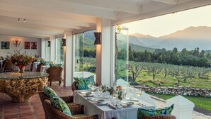 A dining area with a table set for six, overlooking a vineyard and mountains. - Galenia Estate (Montagu)