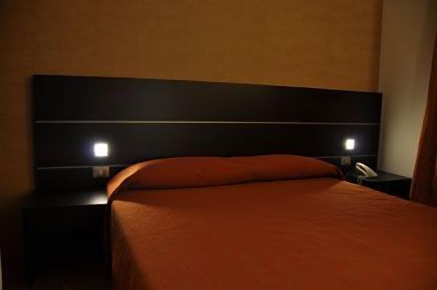Una camera d'albergo con un letto grande, due comodini e un tavolino da notte con una lampada.