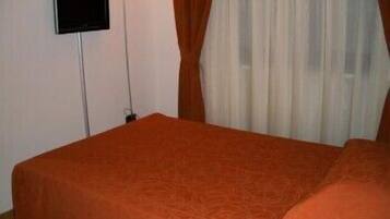 Quarto com cama, televisão na parede e janela com cortinas.