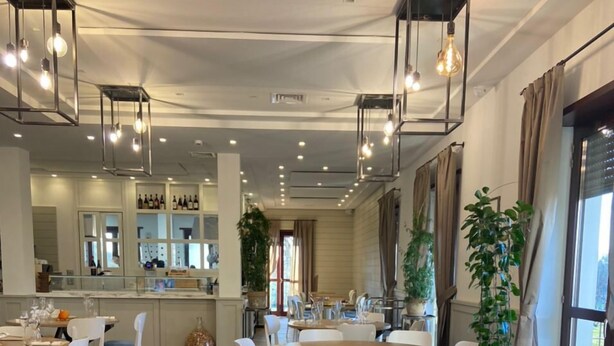 Un moderno comedor con varias mesas y sillas, una zona de bar con estantes llenos de botellas, y amplias ventanas que dejan entrar luz natural.