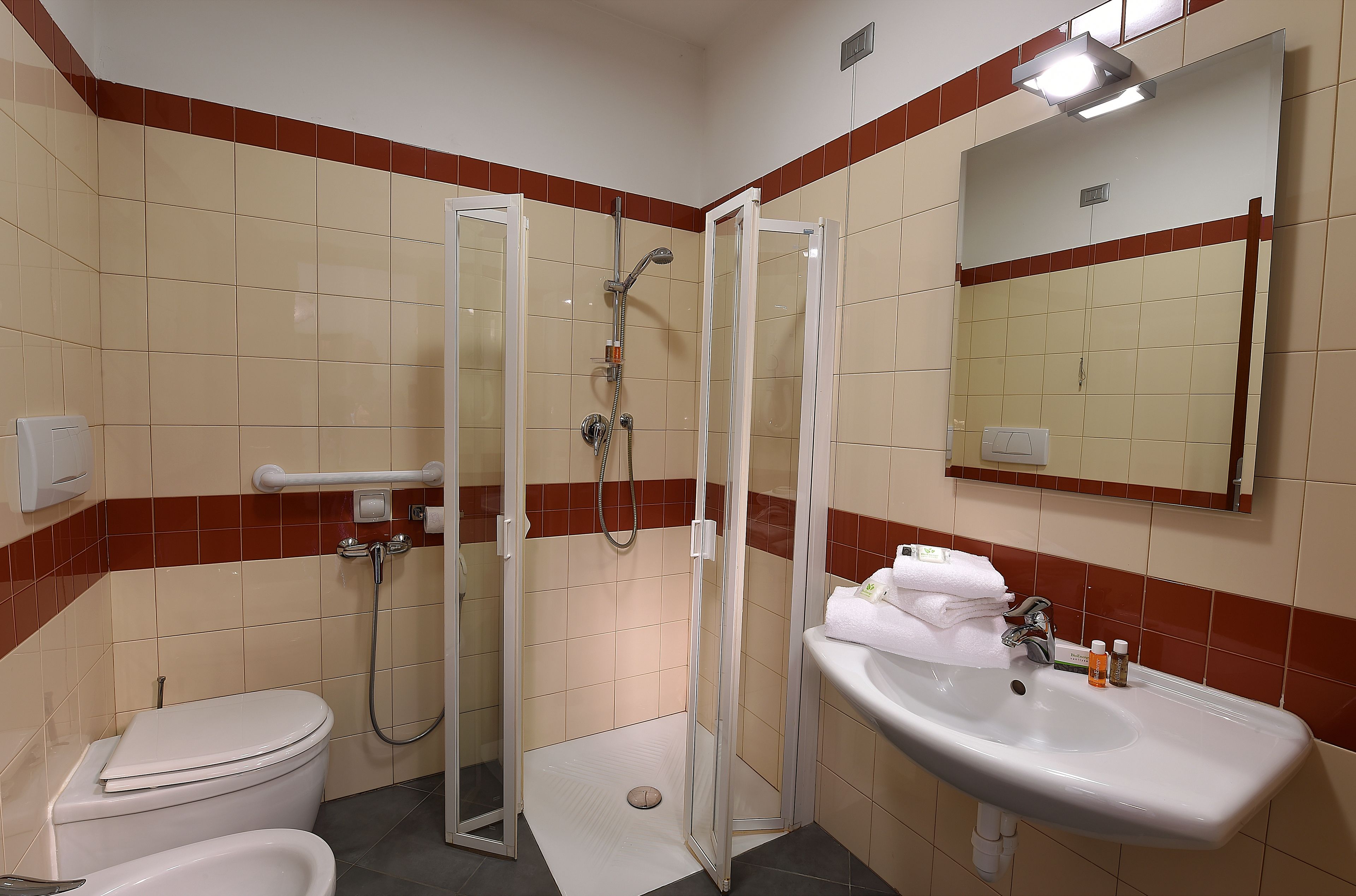 Un baño con inodoro, lavamanos, ducha con puerta de vidrio y espejo.