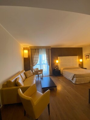 A hotel room with a sofa, a chair, a bed, a nightstand, and a lamp.