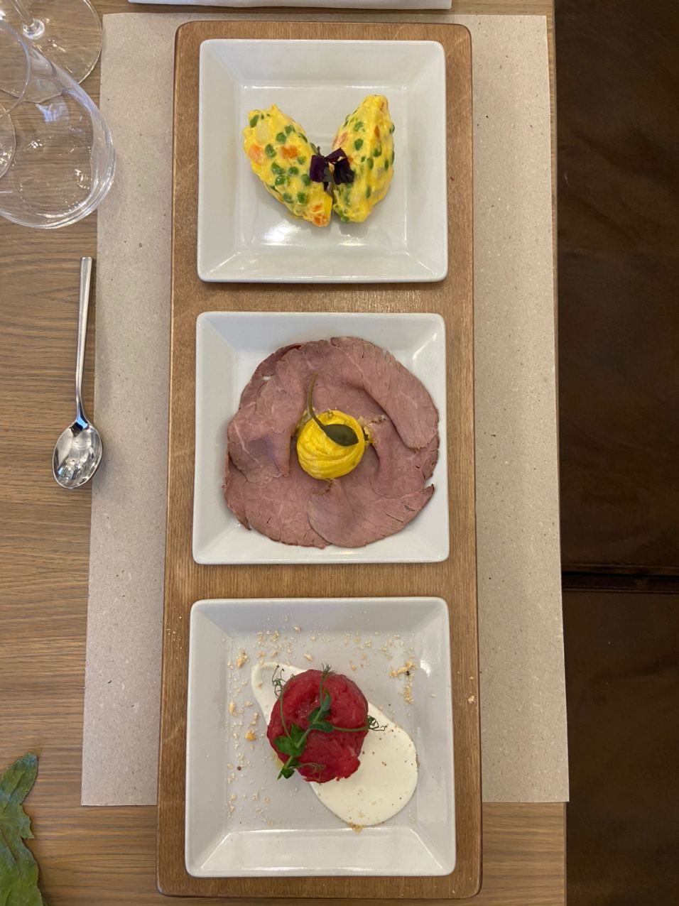 Three square plates of food on a wooden table.
