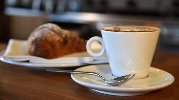 Eine Tasse Kaffee mit Latte-Art auf einem Untertasse, ein Croissant und ein Löffel auf einem Holztisch.