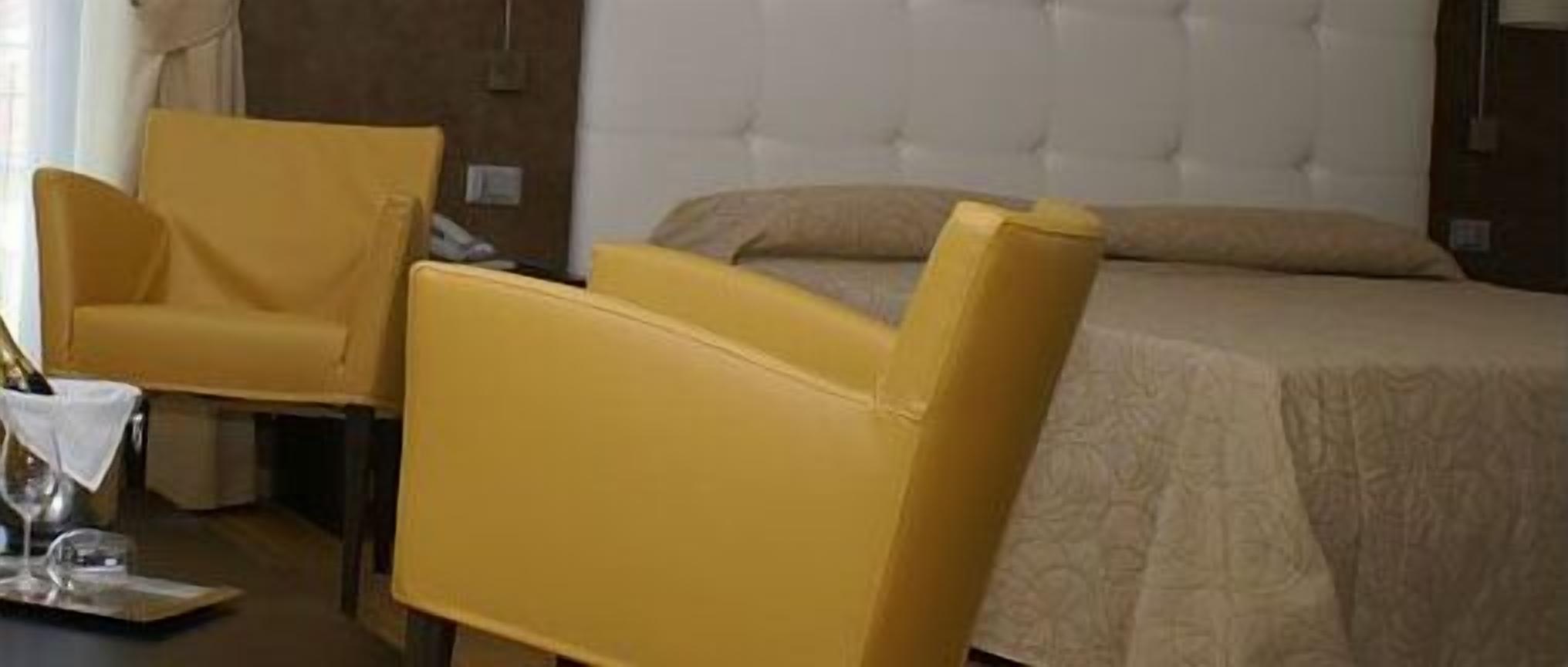 A hotel room with a bed, a yellow armchair, and a small table with a glass and a napkin.