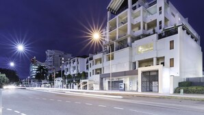 Un edificio moderno de varios pisos con balcones, acceso a nivel de calle y un cartel con la dirección visible.