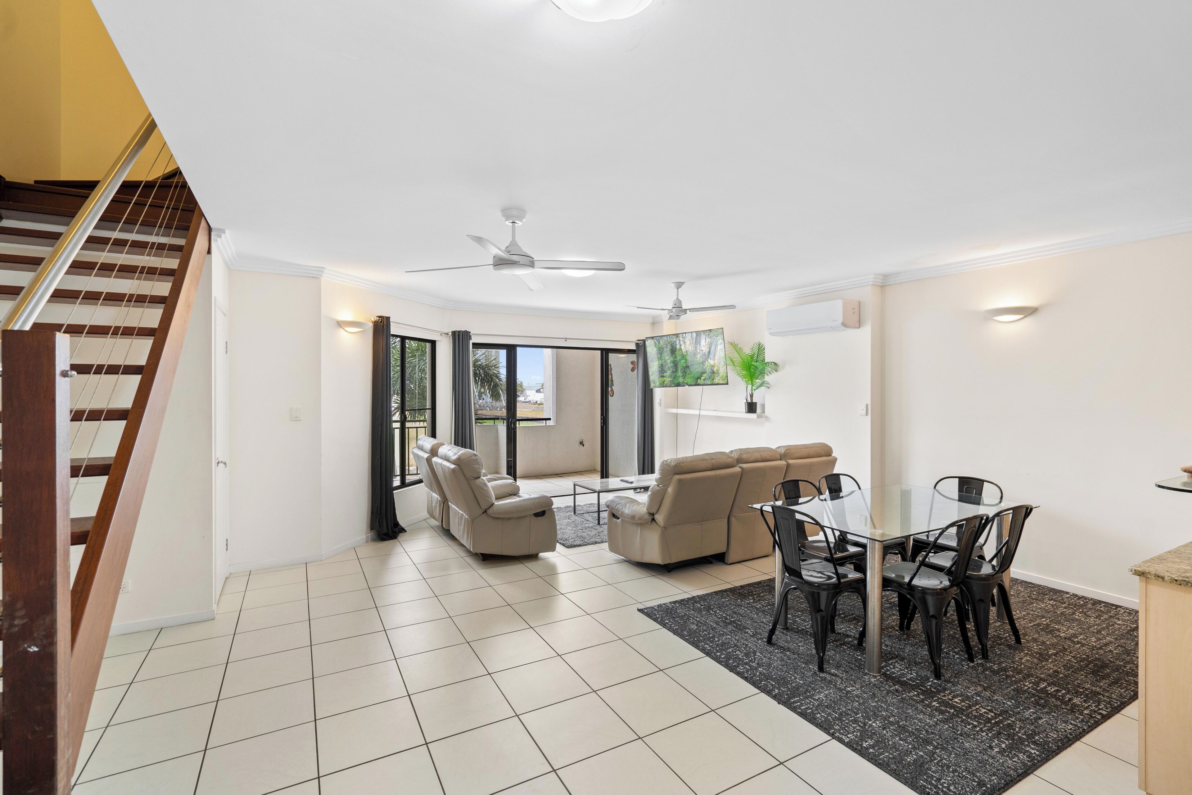 A spacious living area with a sofa set, a dining table with chairs, a ceiling fan, and a TV mounted on the wall.