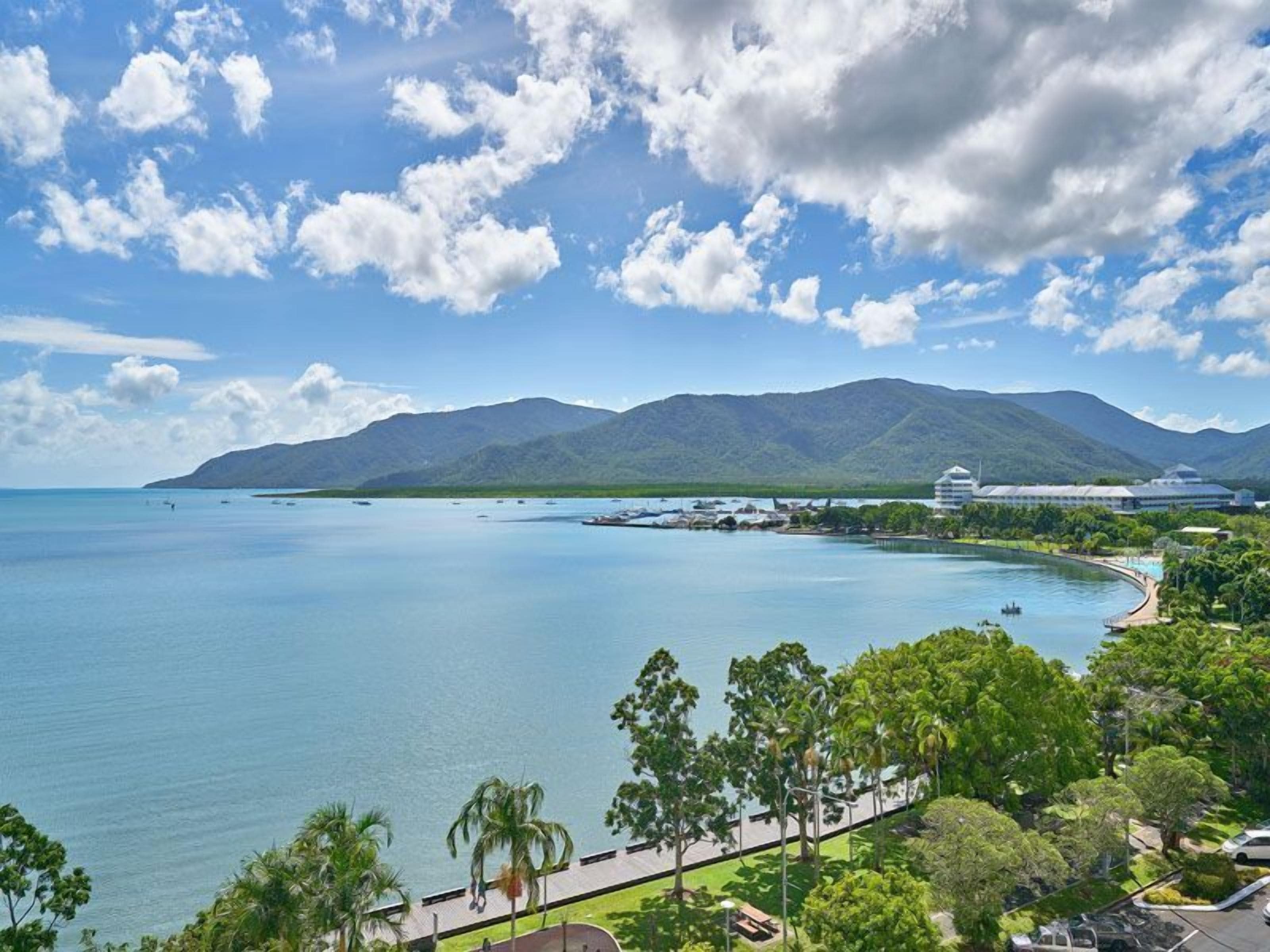 Un resort costero con una piscina grande, palmeras y vistas a las montañas.