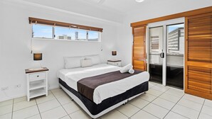 Un dormitorio con cama, mesitas de noche, ventilador de techo, ventana con persianas y puerta corredera de vidrio.