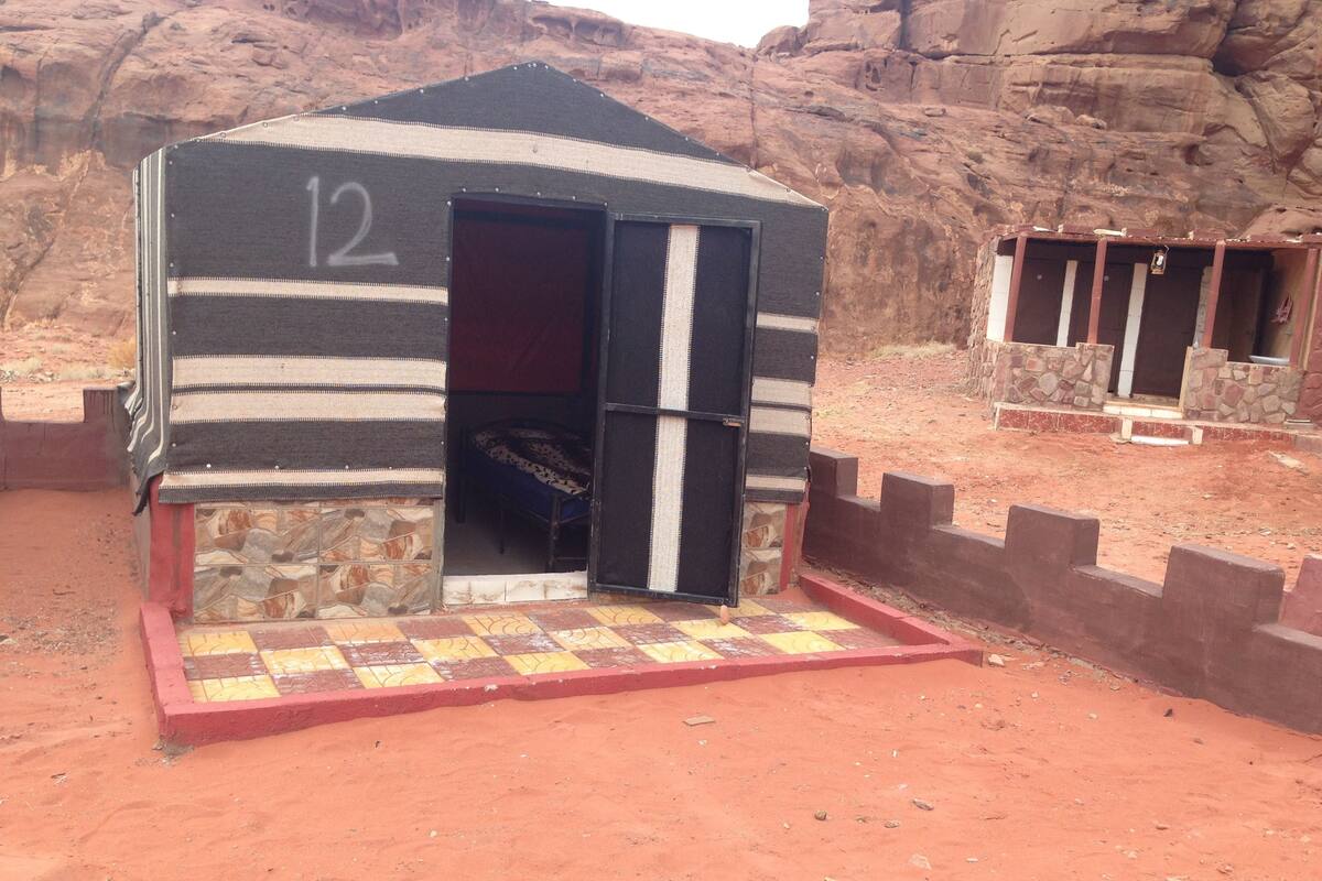 Una pequeña construcción de una sola habitación, con una puerta numerada, una cama y suelo de baldosas de piedra.