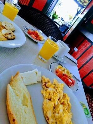 A breakfast setting with plates of scrambled eggs, toast, and fruit, along with glasses of orange juice.