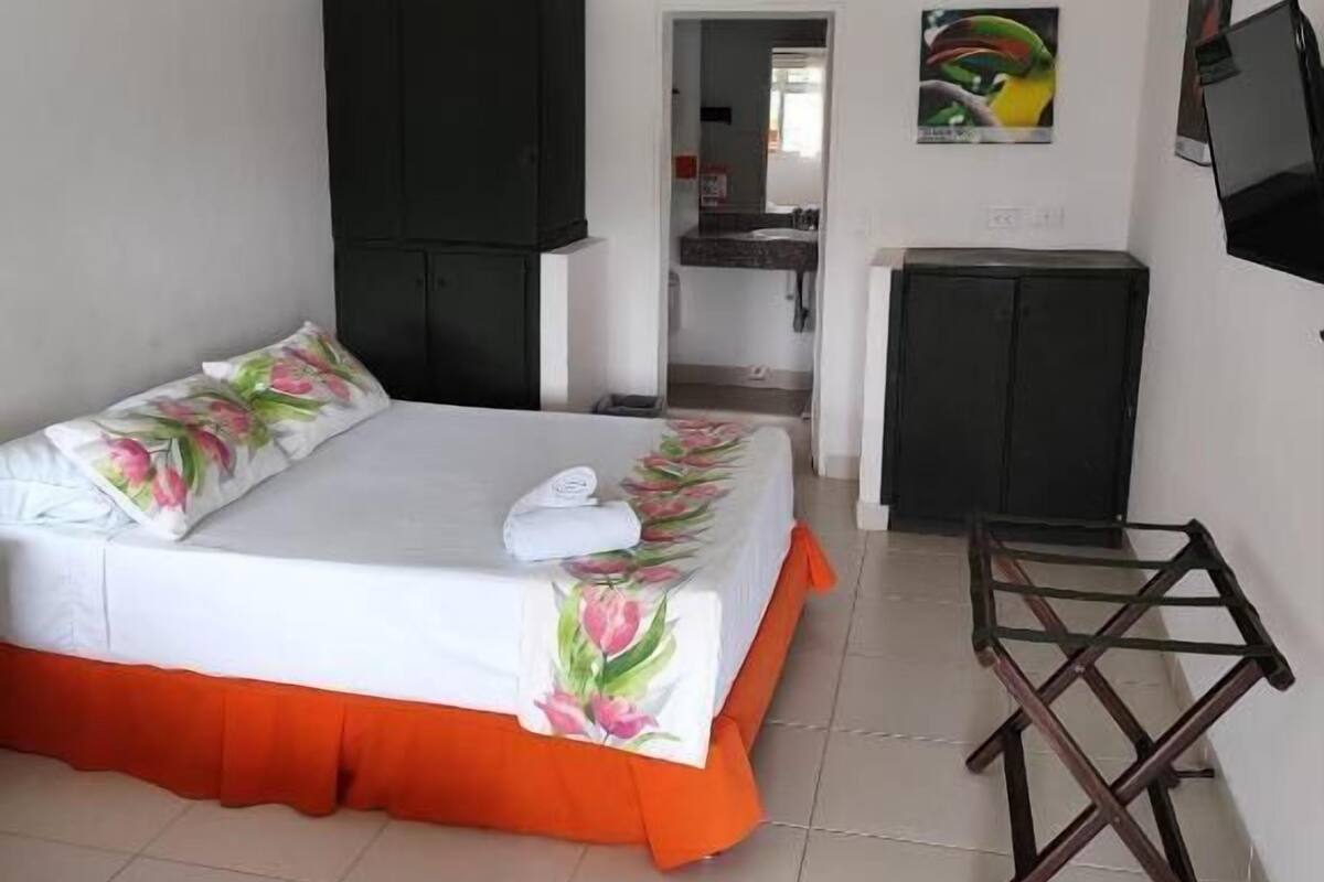 Een hotelkamer met een bed, een bureau, een stoel, een plafondventilator en een televisie aan de muur.