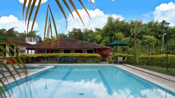 Une piscine dotée d’une terrasse carrelée, entourée de verdure et bordée d’un bâtiment dont le toit est également recouvert de tuiles.
