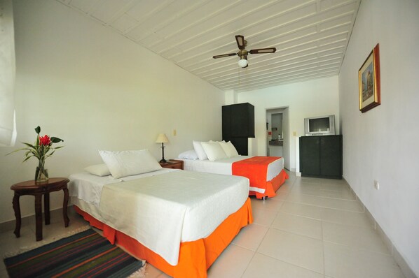 A hotel room with two beds, a ceiling fan, a TV, and a painting on the wall.