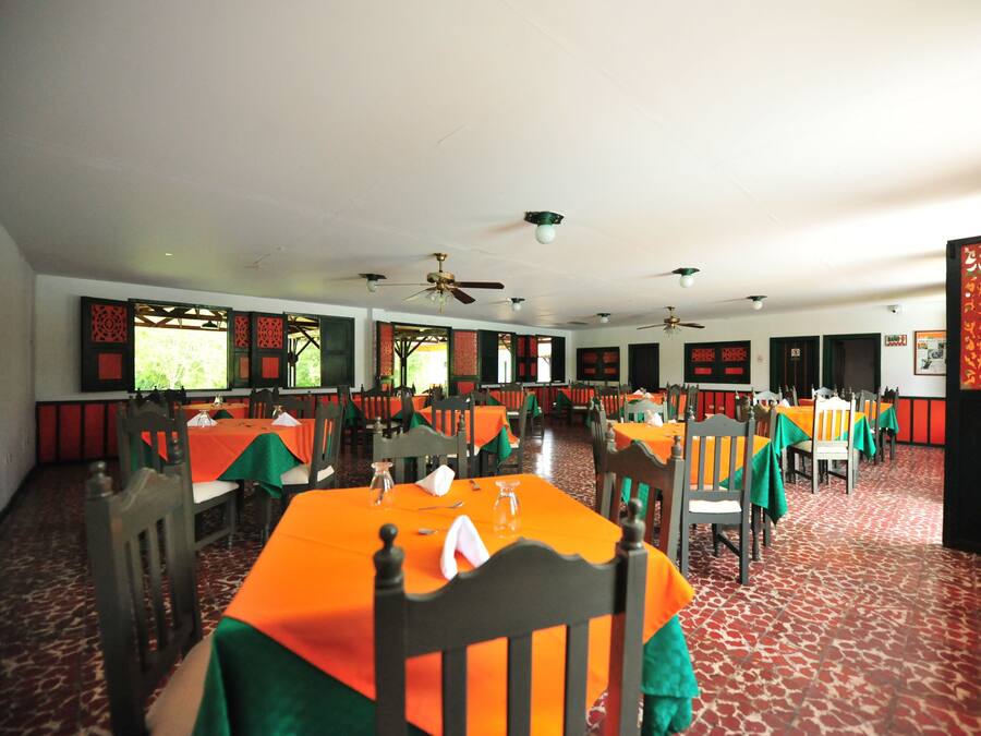 Un espace repas avec des tables recouvertes de nappes orange, des chaises en bois et des ventilateurs de plafond.